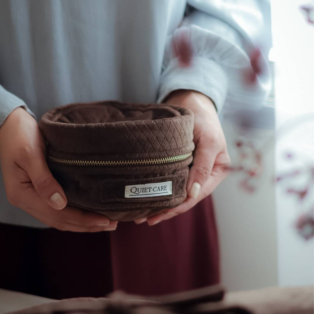 Brown plush pet bed with 'Quiet Care' label held by a person