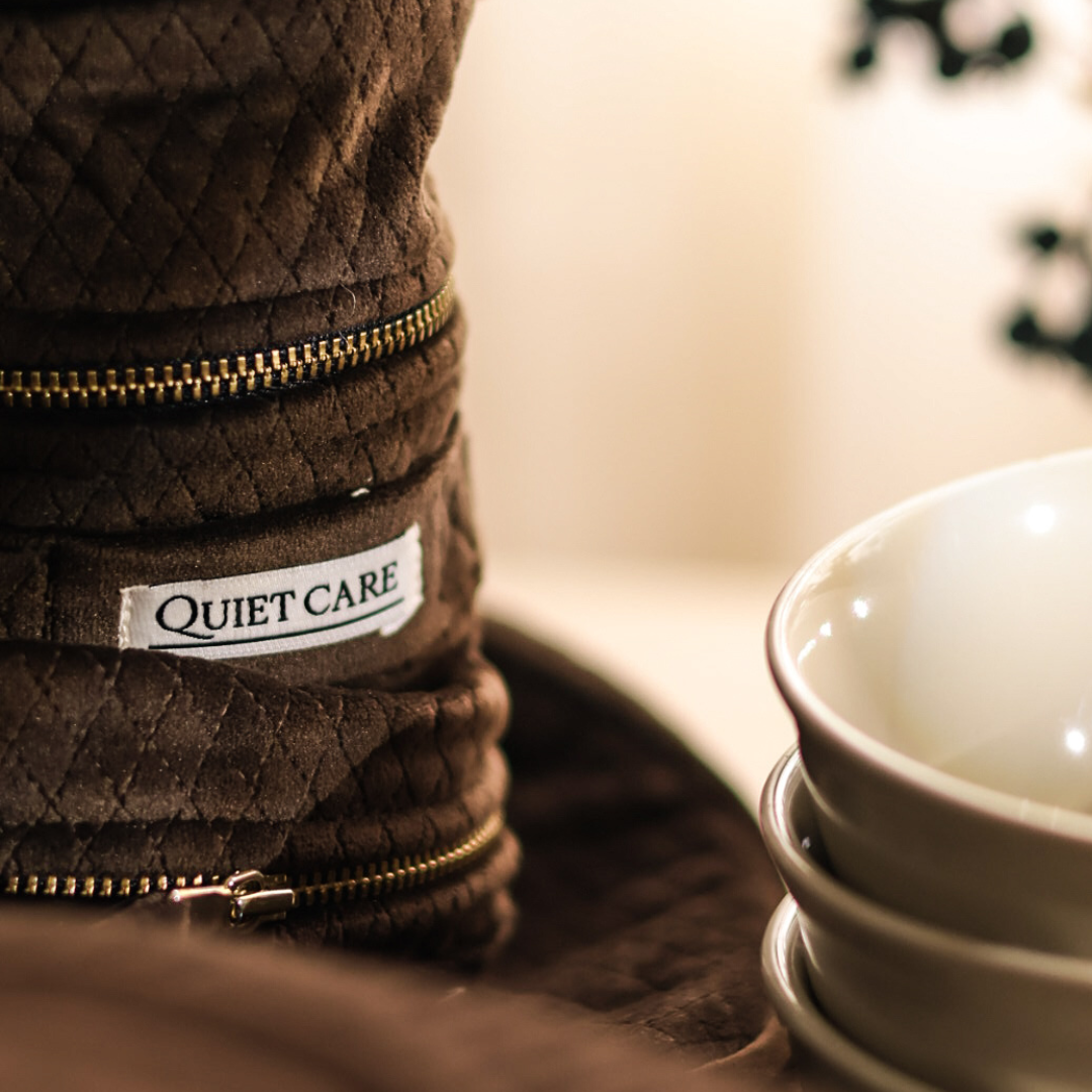 Stack of brown quilted bags with 'Quiet Care' label next to a white bowl.