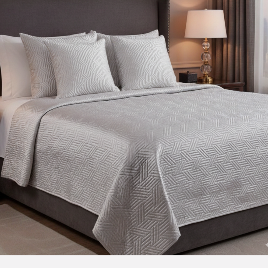 Bed with gray geometric patterned comforter and pillows in a bedroom setting.