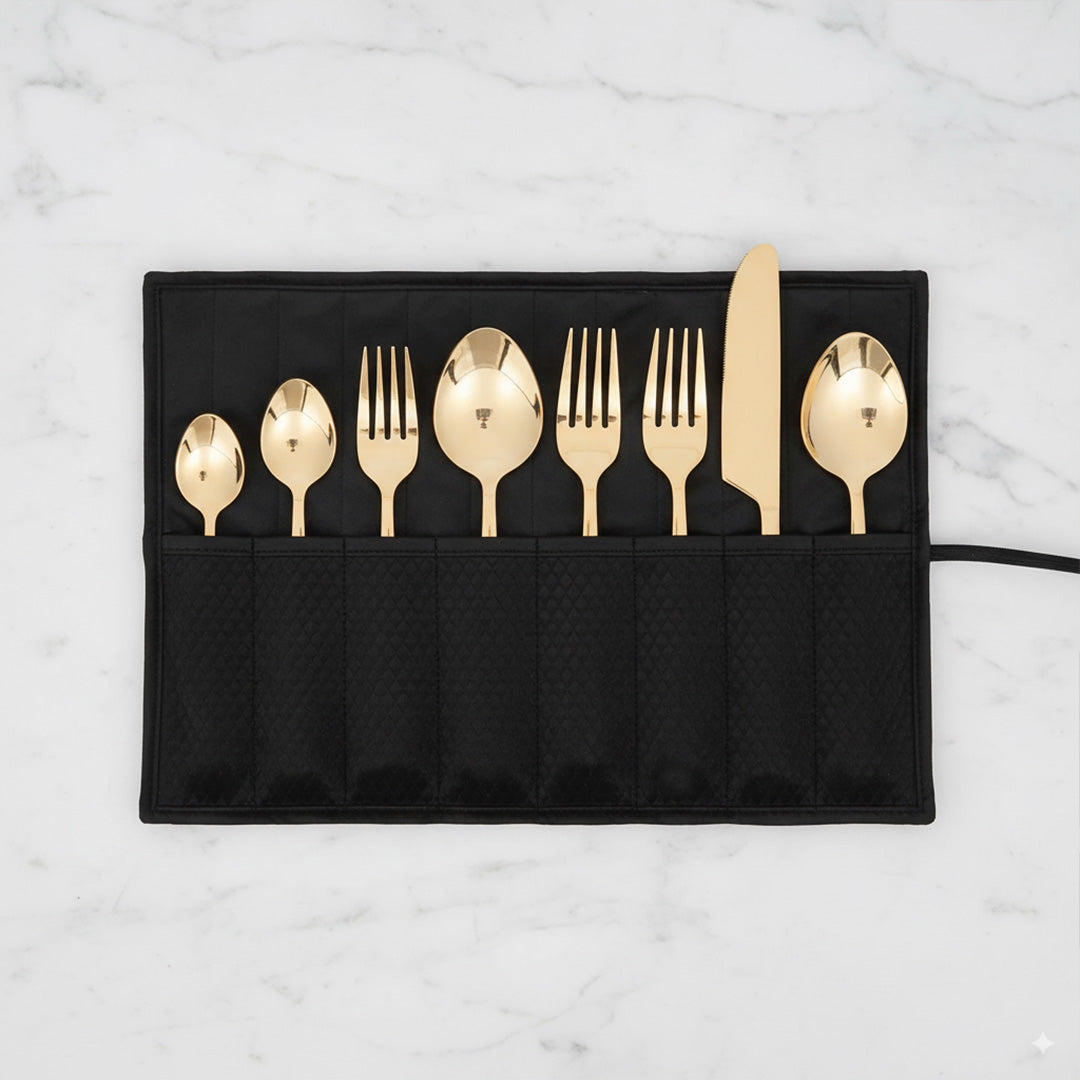 Set of gold cutlery including spoons and forks on a black placemat against a marble background.