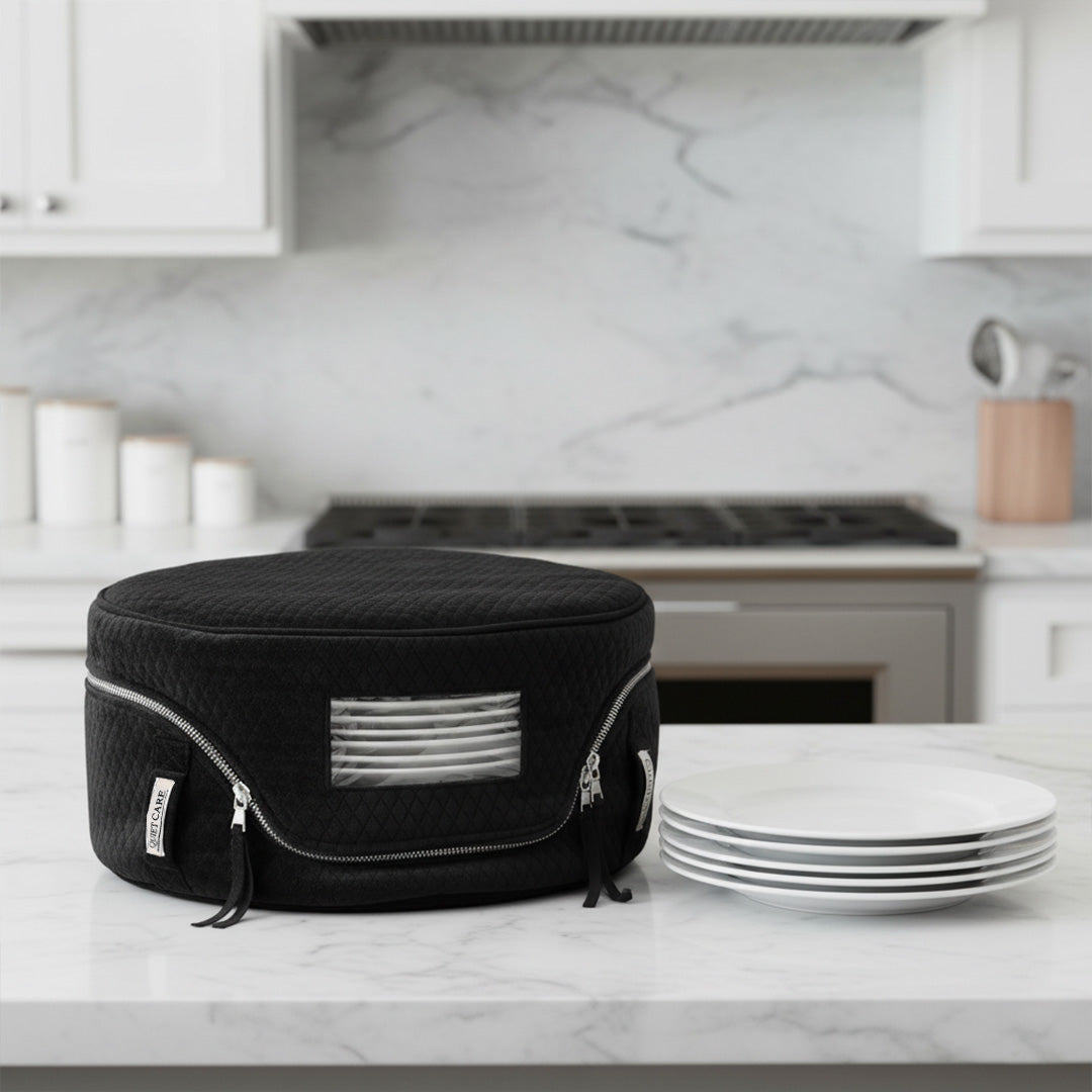 Black insulated food carrier on a kitchen counter with white plates in the background