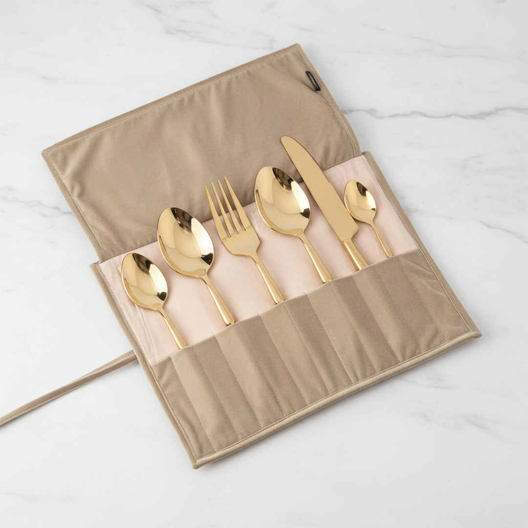 Set of gold cutlery including spoons and a knife on a beige carrying case against a white marble background.