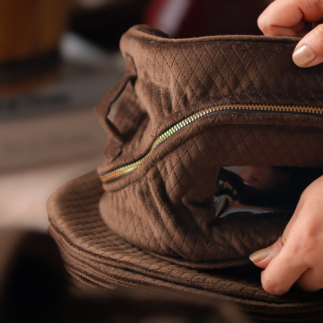 Brown quilted bag with a zipper held by a hand against a blurred background