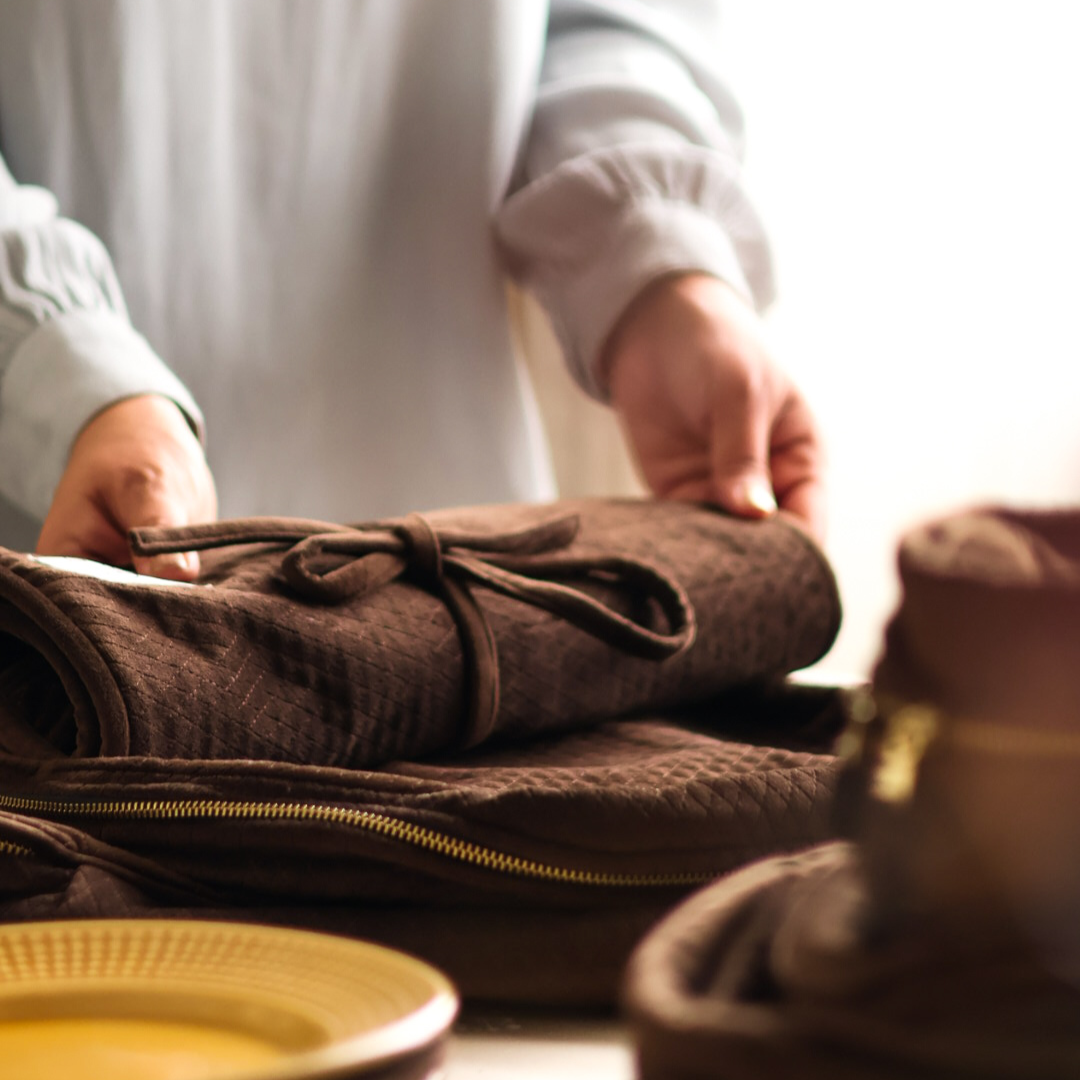 Person folding a brown fabric item on a table with a blurred background