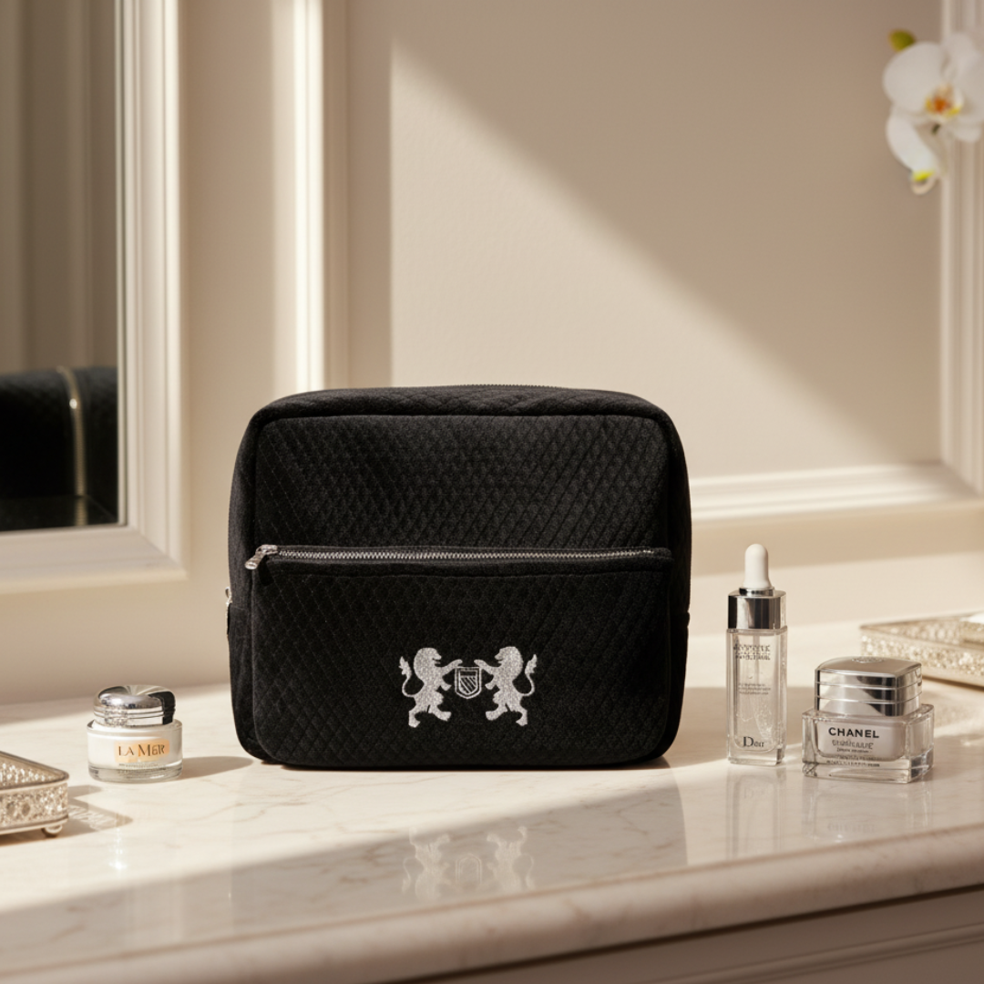 Black quilted toiletry bag with a logo on a marble surface with skincare products.