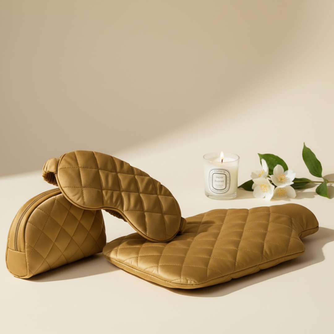 Pair of quilted brown slippers on a beige surface with a candle and flowers in the background.